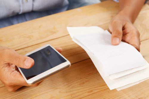 Closeup of woman calculating or paying bills. Person using smartphone. Online payment concept. Cropped view.